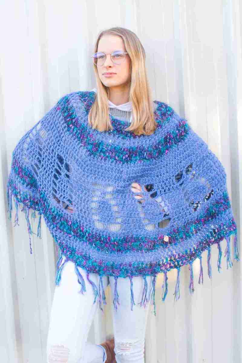 Pineapple Poncho Crochet Pattern – Blue version on Model against white wall with hands on hips Pineapple Poncho Crochet Pattern - Blue version on Model against white wall with hands on hips