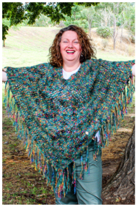 Fiona Langtry, Chief Crochet Designer & CEO for ReVeDesignCo wearing a multicolored green poncho with arms open wide and big smile. Eyes are closed. Welcome! Start here and join me in this blogging journey
