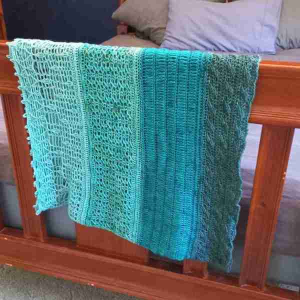Ocean Layers Wrap Crochet Pattern by ReVeDesignCo - hanging at the end of a bed - in shades of teal