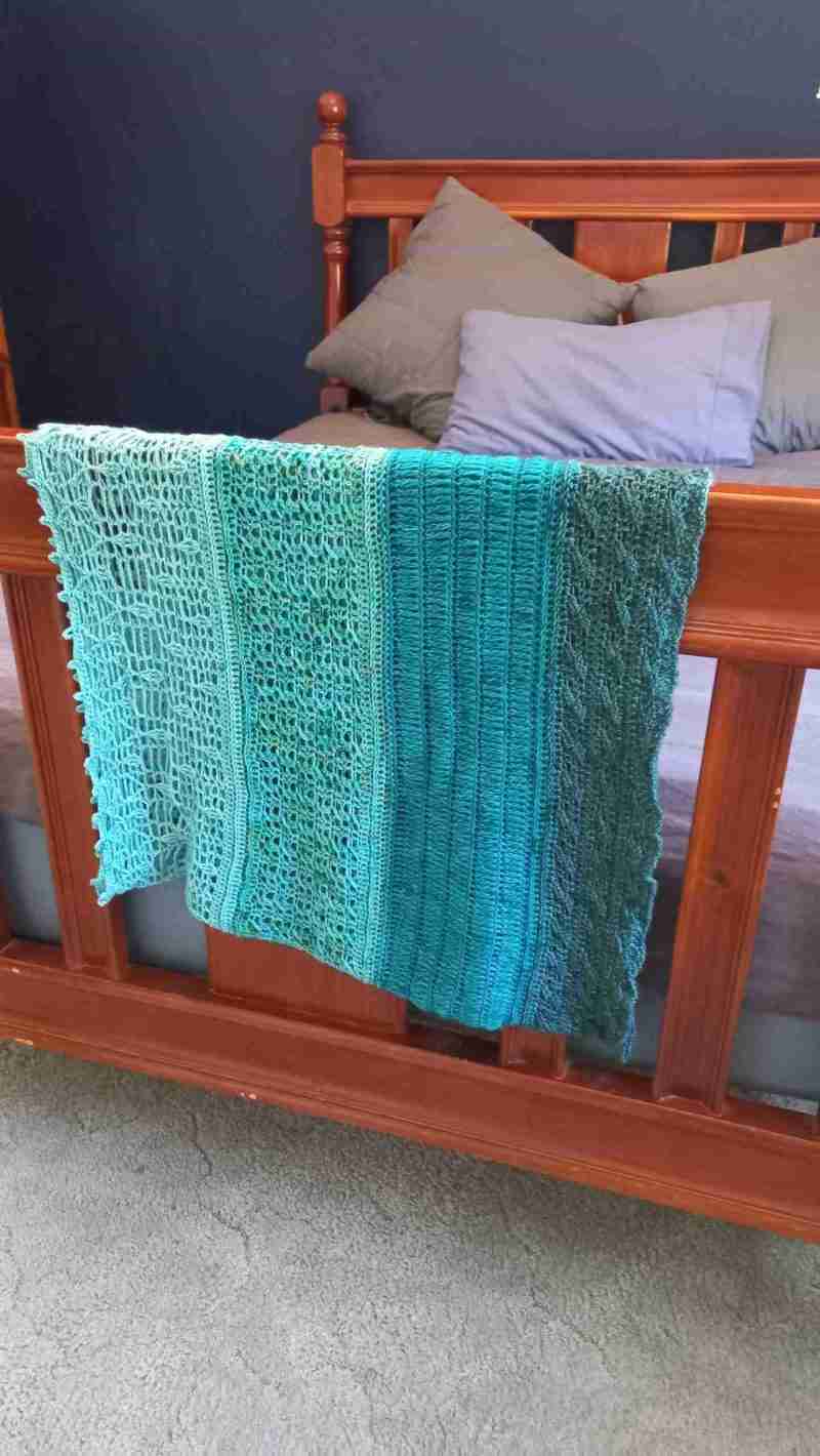 Ocean Layers Wrap Crochet Pattern by ReVeDesignCo - hanging at the end of a bed - in shades of teal
