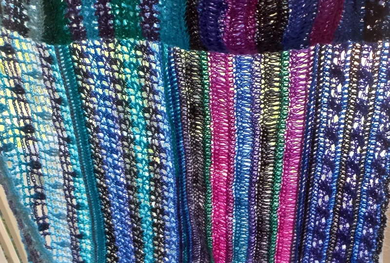 Ocean Layers Wrap Crochet Pattern by ReVeDesignCo - hanging outside with light shining through showing the details - Multicolored Sock Yarn version