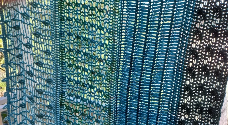 Ocean Layers Wrap Crochet Pattern by ReVeDesignCo - hanging outside with light shining through showing the details - in shades of teal
